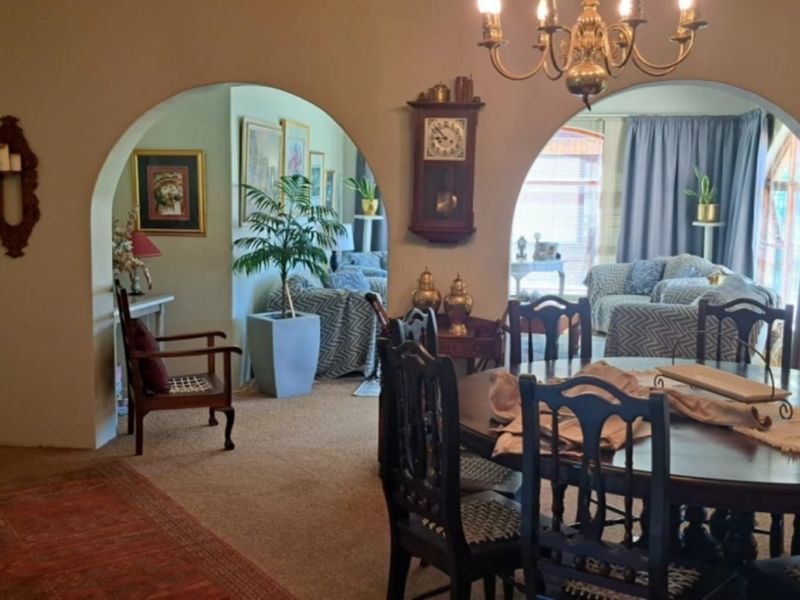 A traditional dining room featuring distinctive arched doorways leading to adjacent living spaces, illuminated by a classic chandelier.