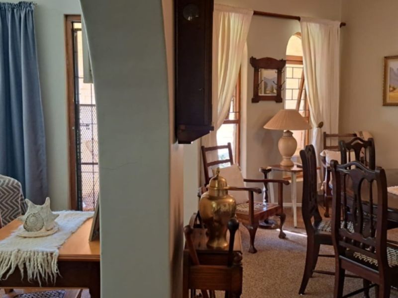 A traditional living and dining area featuring an arched architectural transition, large windows, and carpeted flooring.