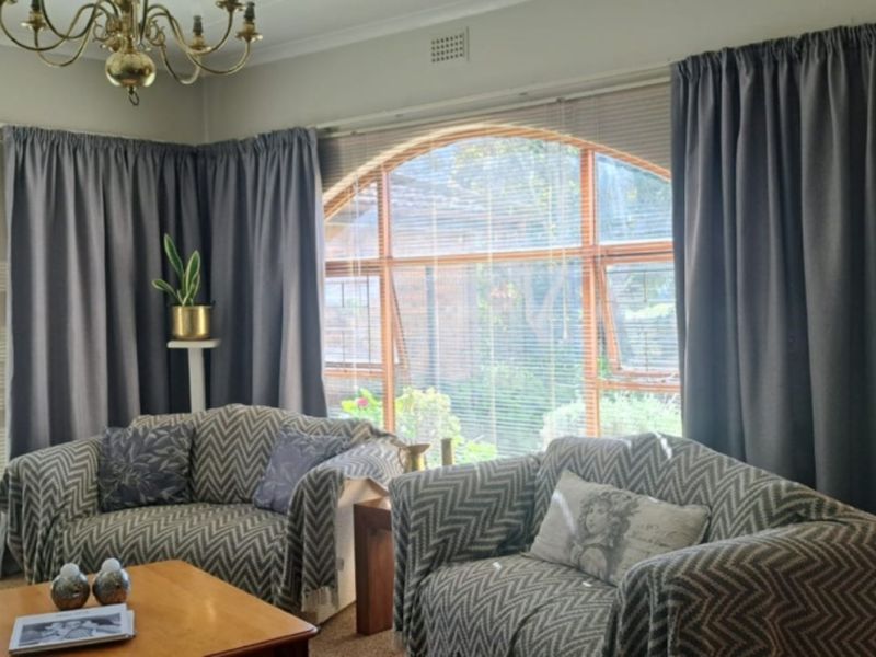 A living room featuring large arched windows, a classic chandelier, and a security gate, offering a bright and traditional living space.