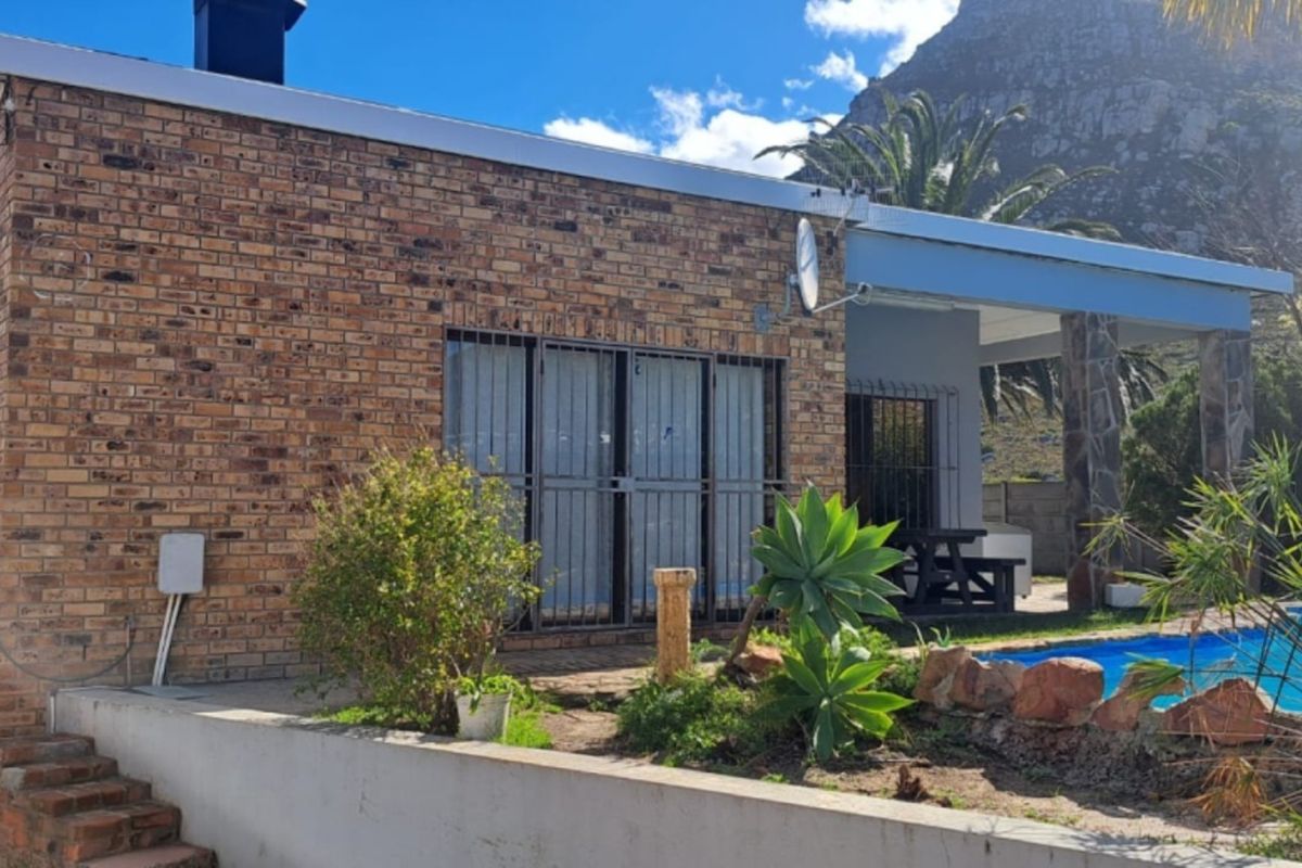 Rear exterior view of the property featuring a face brick facade, a covered patio area, and a private swimming pool set against a mountain backdrop.