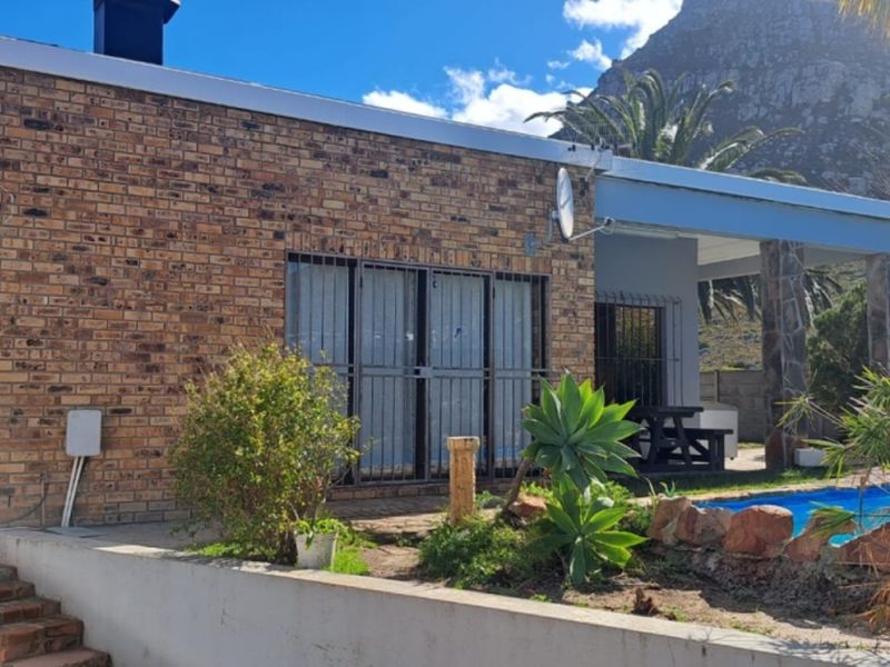Rear exterior view of the property featuring a face brick facade, a covered patio area, and a private swimming pool set against a mountain backdrop.
