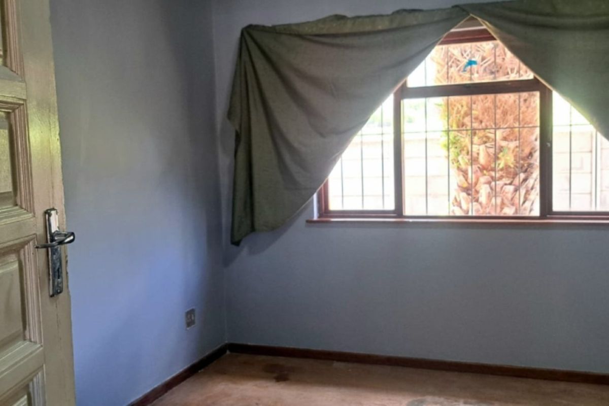 An empty bedroom featuring a timber door, security bars on the window, and worn flooring, offering a blank canvas for renovation.