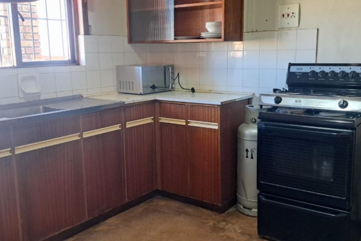 A dated kitchen featuring original laminate cabinetry, a stainless steel sink, tiled splashbacks, and a freestanding gas stove.