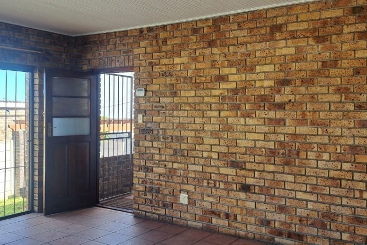 An empty living area featuring exposed brick walls, tiled flooring, and direct access to the exterior through a sliding glass door.