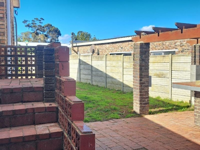Rear garden area featuring a brick-paved patio, built-in braai, timber pergola, and decorative brick screening walls.
