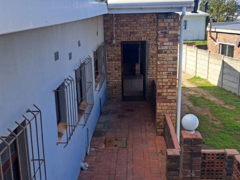 Rear exterior view of the property featuring a brick-paved walkway, security bars on windows, and a surrounding precast concrete boundary wall.
