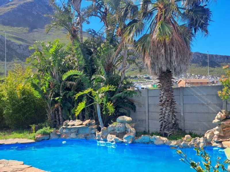 Outdoor pool area featuring a rock water feature, established garden landscaping, and mountain views, enclosed by a precast concrete boundary wall.