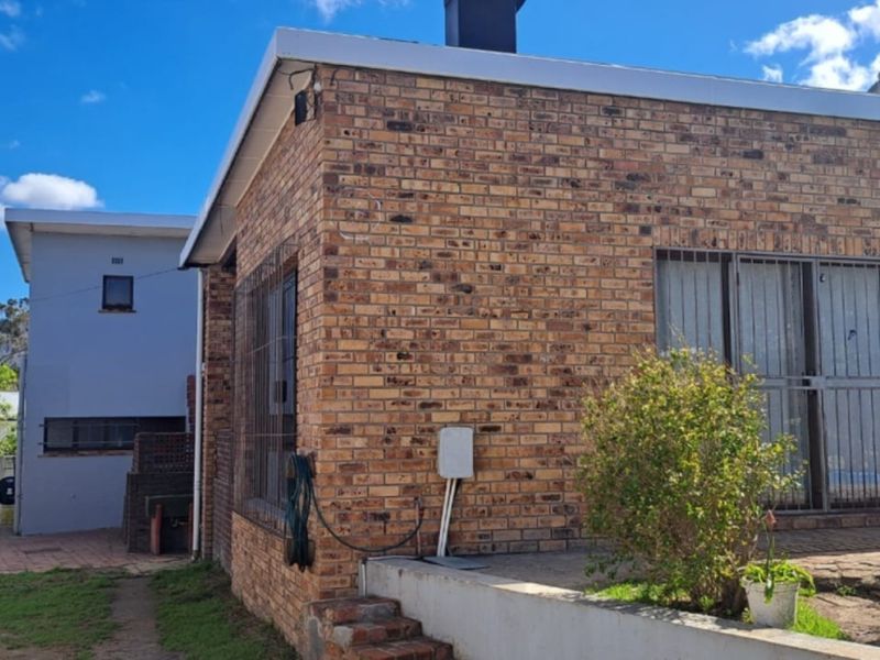 Rear view of the property featuring face brick exterior, security bars on windows, a paved patio area, and a built-in outdoor braai.