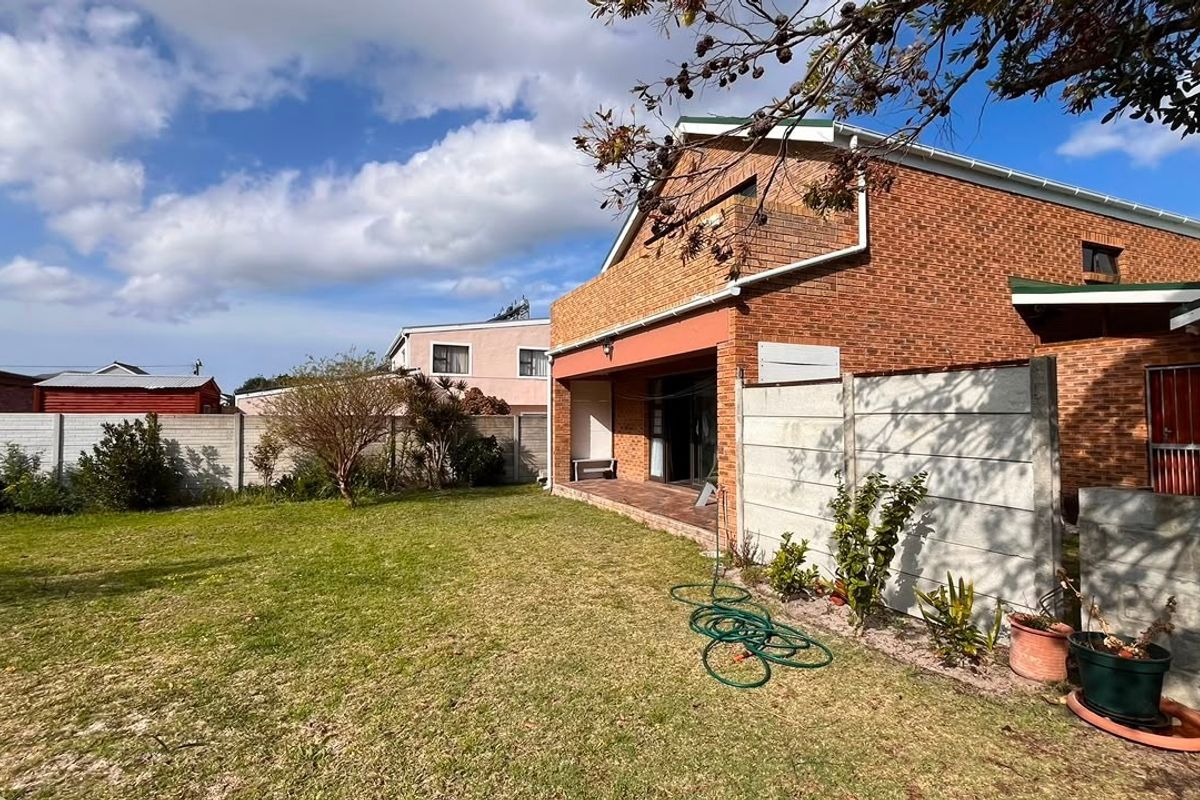 Rear view of the property featuring a brick facade, a covered patio area, and a spacious garden enclosed by precast concrete boundary walls.