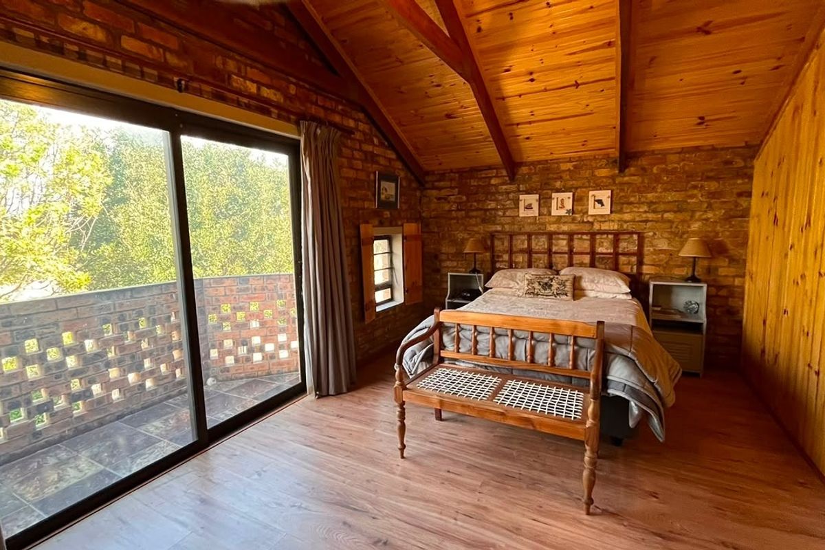 A rustic bedroom featuring exposed brick walls, a high timber vaulted ceiling, laminate flooring, and a sliding glass door leading to a private balcony.