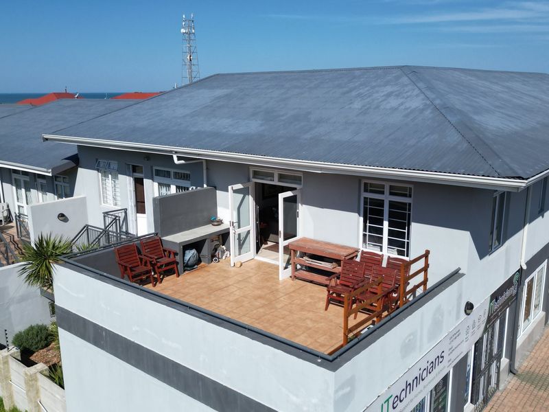 An elevated balcony featuring tiled flooring and a built-in braai area, providing outdoor space with views of the surrounding property and coastline.