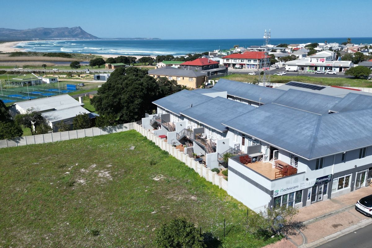 Aerial view of the apartment complex featuring a metal roof, ground-level commercial space, and proximity to the coastline and local amenities.