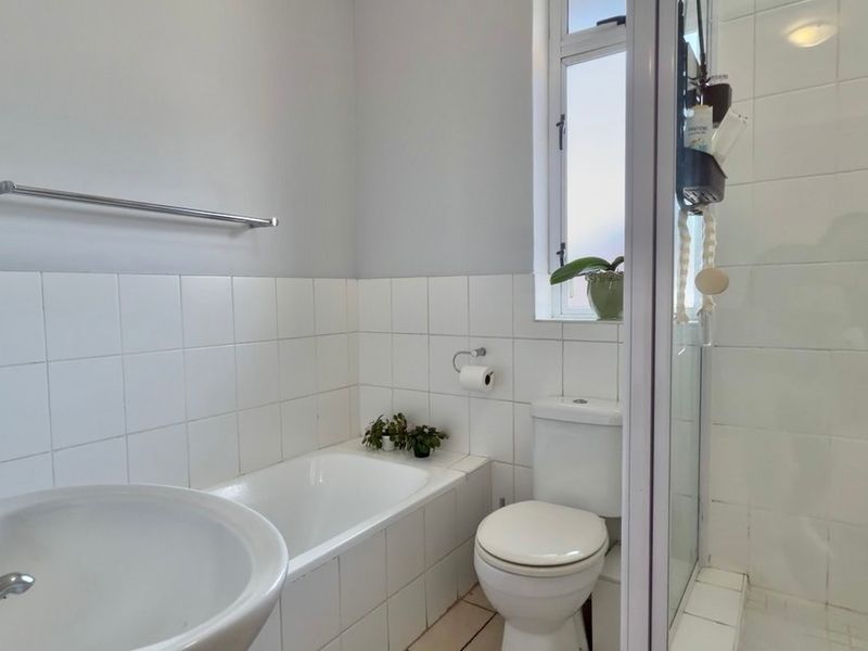 A functional bathroom featuring a built-in bathtub, separate shower enclosure, pedestal washbasin, and toilet with white tiled finishes.