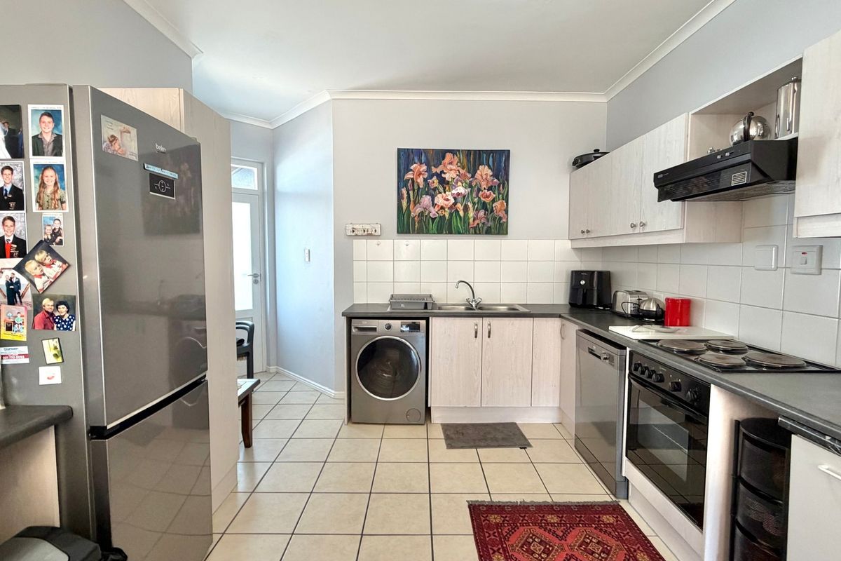 A functional kitchen featuring light-toned cabinetry, tiled backsplash, integrated oven and hob, and tiled flooring with direct access to an adjacent area.