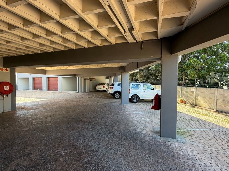 A covered parking area featuring a concrete waffle ceiling, paved flooring, and secure perimeter fencing.