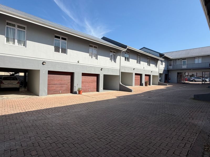 Exterior view of an apartment complex featuring a paved courtyard, multiple garage doors, covered parking areas, and upper-level balconies.