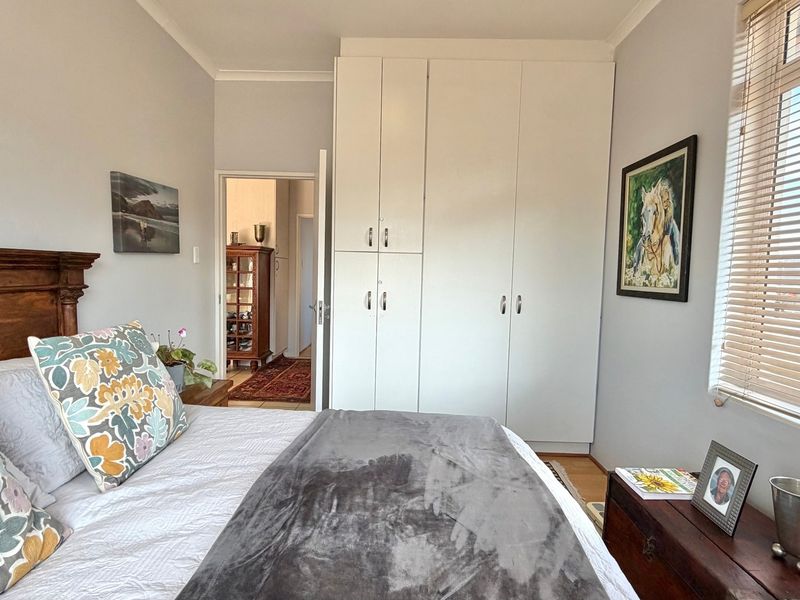 A well-maintained bedroom featuring ample built-in cupboard storage, neutral wall finishes, and natural light provided by a window with fitted venetian blinds.