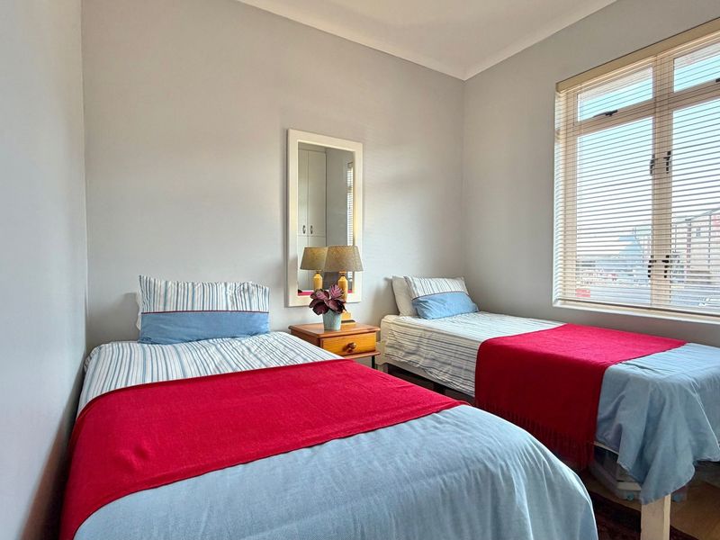 A functional bedroom featuring neutral wall finishes, coving, and a large window fitted with venetian blinds.