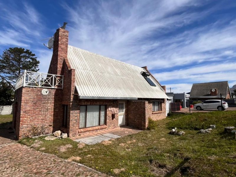 Front view of a brick-clad house featuring a steep corrugated metal roof, a prominent chimney, and an upper-level balcony.
