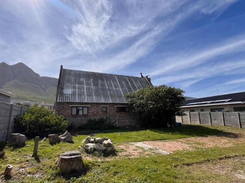 Rear view of a brick house featuring a corrugated roof, set within a garden with boundary walls and mountain views.