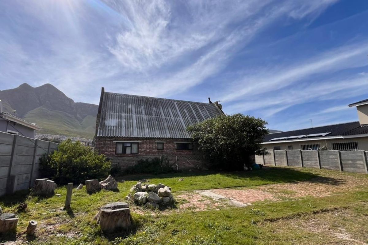 Rear view of a brick house featuring a corrugated roof, set within a garden with boundary walls and mountain views.