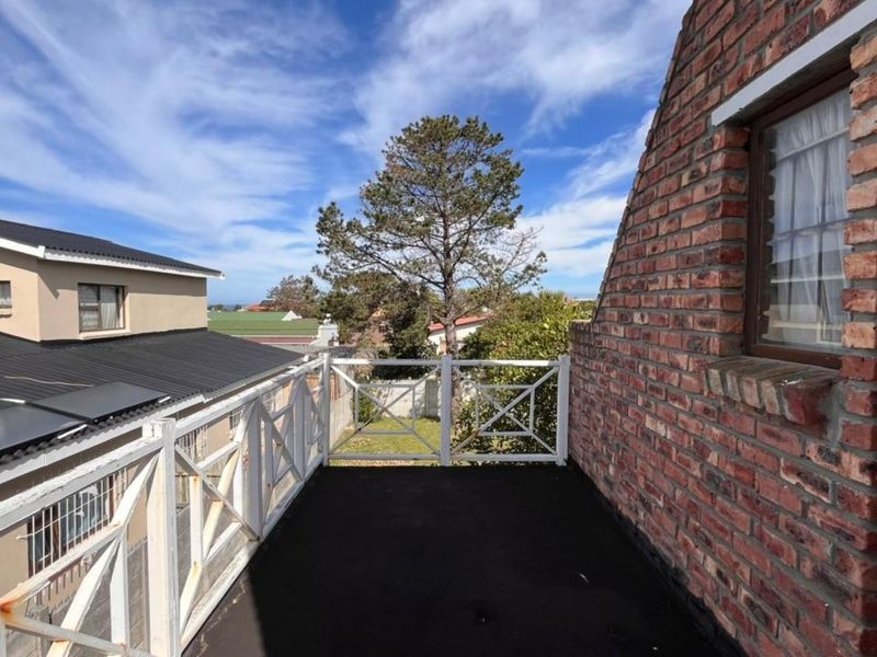 An elevated balcony featuring exposed brickwork and a white timber balustrade, offering an outdoor space with views of the surrounding neighborhood.