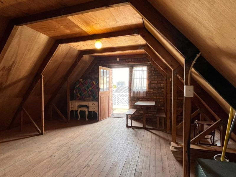 Attic-style bedroom featuring exposed timber rafters, brick wall accents, and wooden flooring with direct access to an outdoor area.