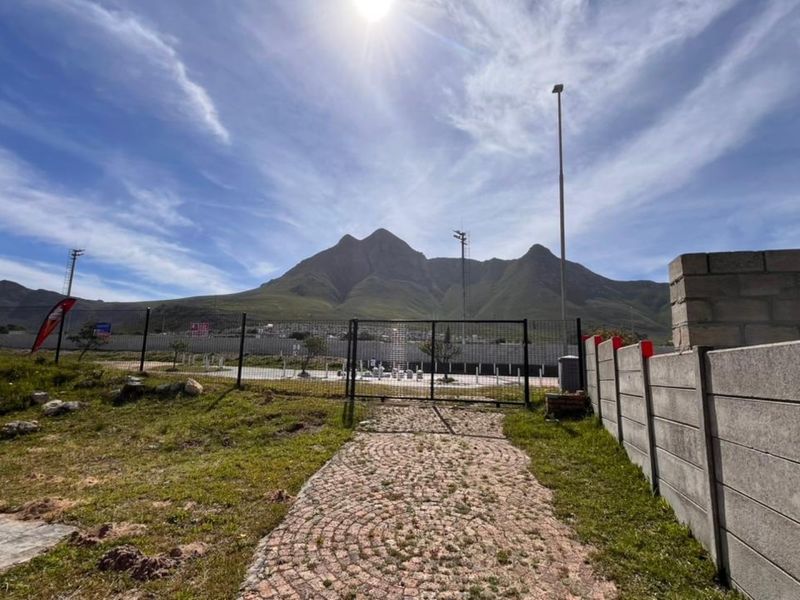 Outdoor area featuring a paved walkway, metal security gate, and precast boundary wall with a scenic mountain backdrop.
