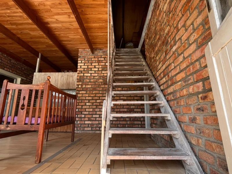 A covered patio area featuring exposed brick walls, a timber ceiling, and a wooden staircase leading to an upper level.