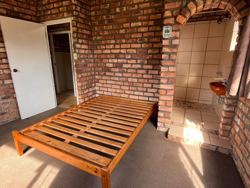 Bedroom featuring exposed brick walls, carpeted flooring, and an open-plan en-suite bathroom with a shower and pedestal basin.