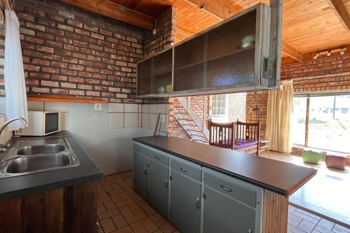 Rustic kitchen featuring exposed brick walls, timber ceilings, and a functional layout with double sink and built-in cabinetry.