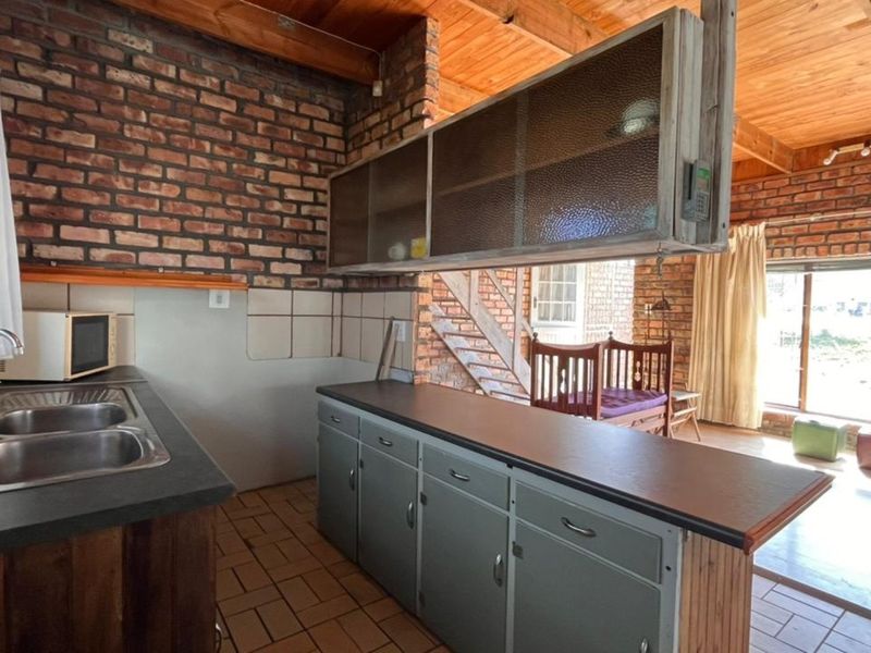 Rustic kitchen featuring exposed brick walls, timber ceilings, and a functional layout with double sink and built-in cabinetry.
