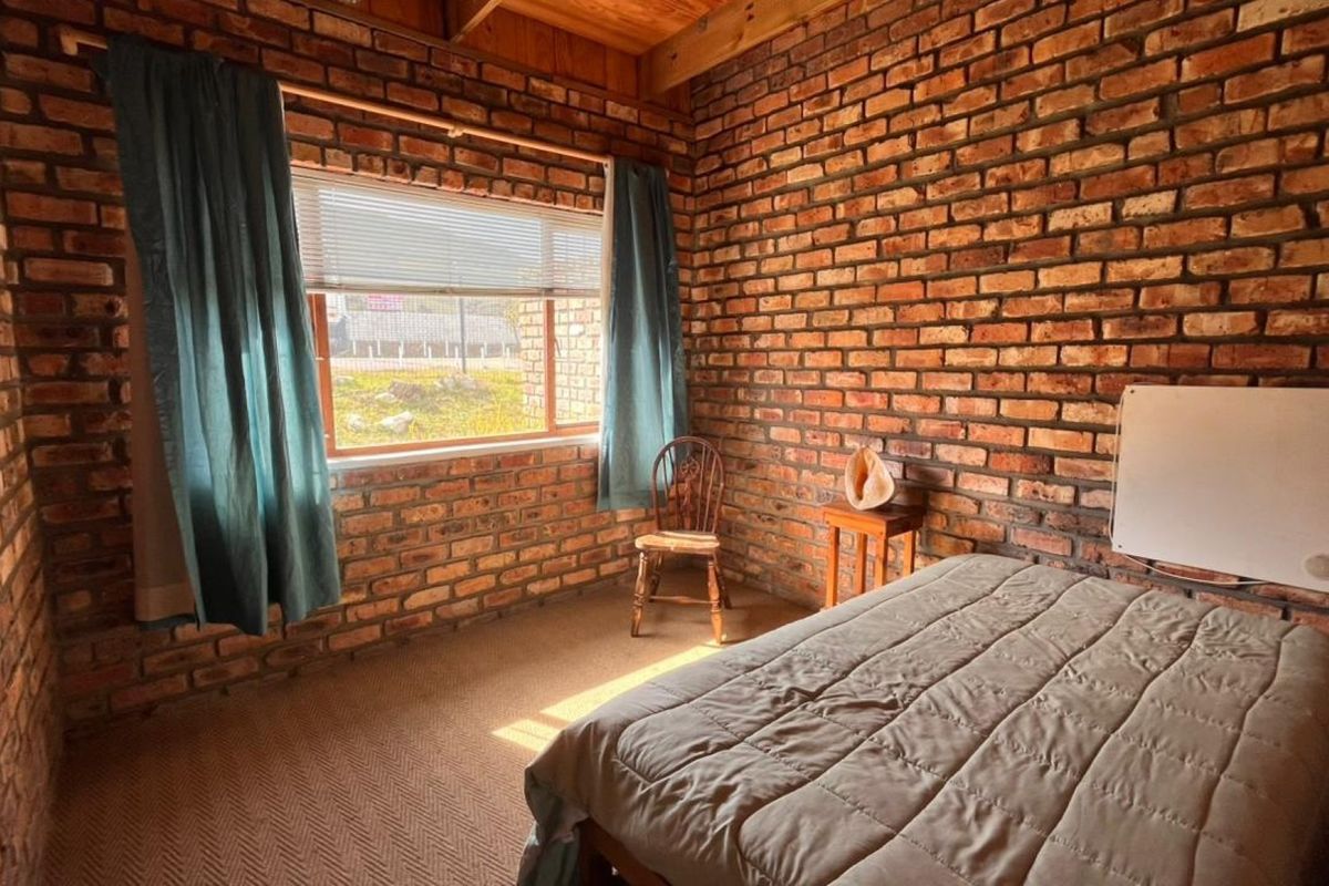 A rustic bedroom featuring exposed brick walls, timber ceiling beams, and carpeted flooring, offering a warm and textured aesthetic.