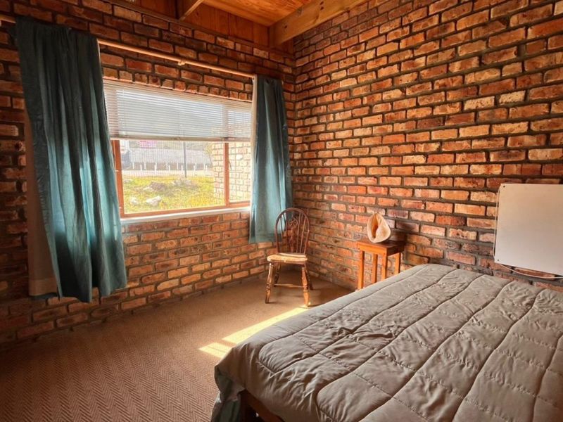 A rustic bedroom featuring exposed brick walls, timber ceiling beams, and carpeted flooring, offering a warm and textured aesthetic.