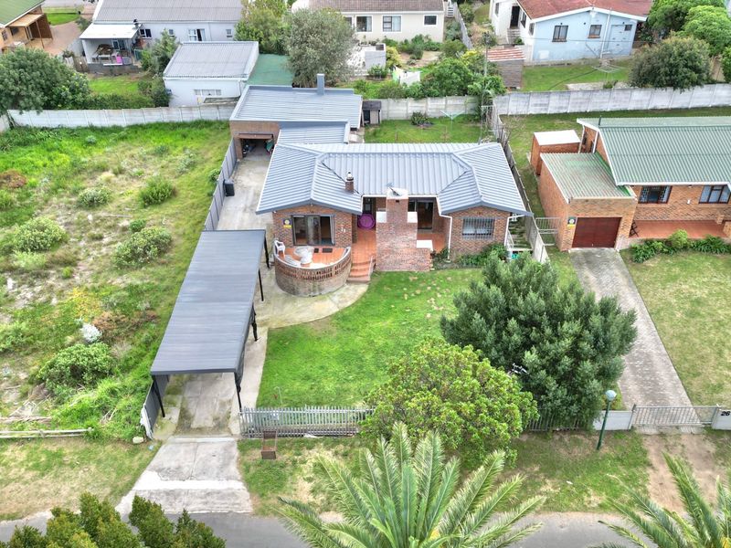 Aerial view of a residential property featuring a brick house with a metal roof, a carport, and a spacious garden area.