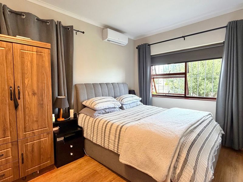 A well-maintained bedroom featuring laminate flooring, a wall-mounted air conditioning unit, and a window fitted with security bars.
