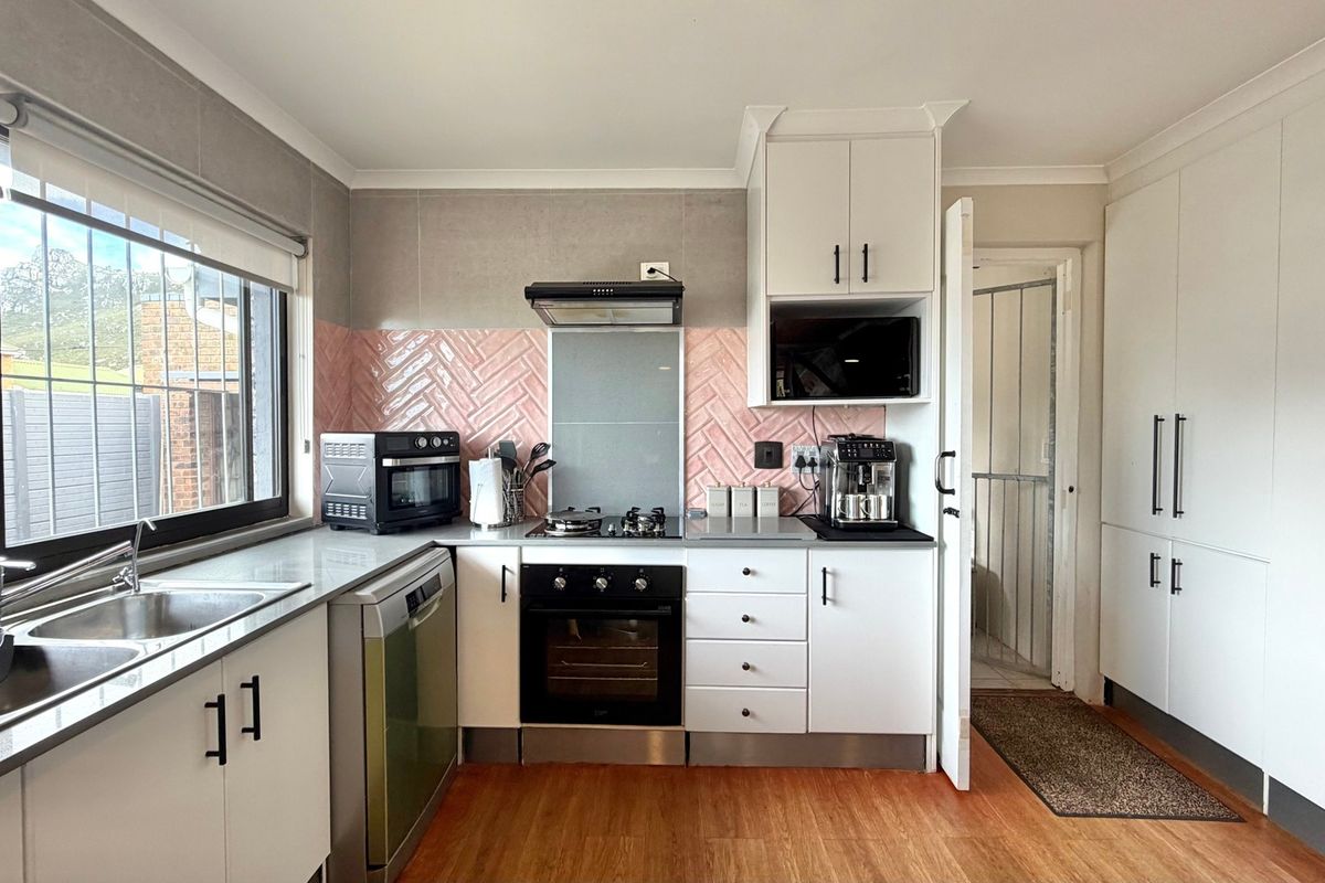 A well-maintained kitchen featuring white cabinetry, a herringbone-patterned pink tiled backsplash, stainless steel sink, and integrated gas hob with oven.