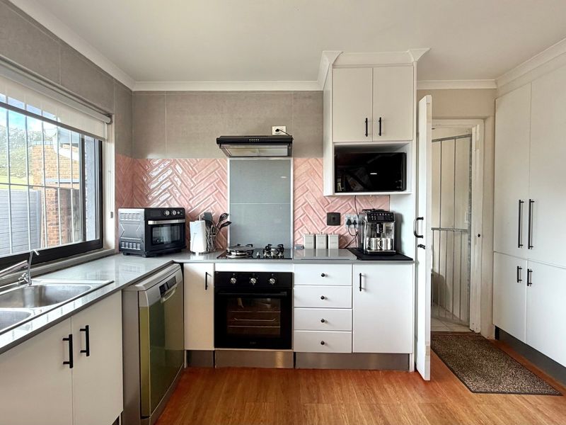 A well-maintained kitchen featuring white cabinetry, a herringbone-patterned pink tiled backsplash, stainless steel sink, and integrated gas hob with oven.