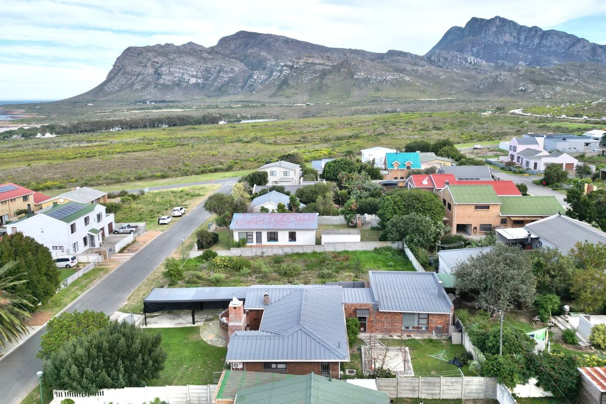 Aerial view of the property showing the main dwelling with a metal roof, brick exterior, carport, and surrounding residential neighborhood with mountain and coastal views.