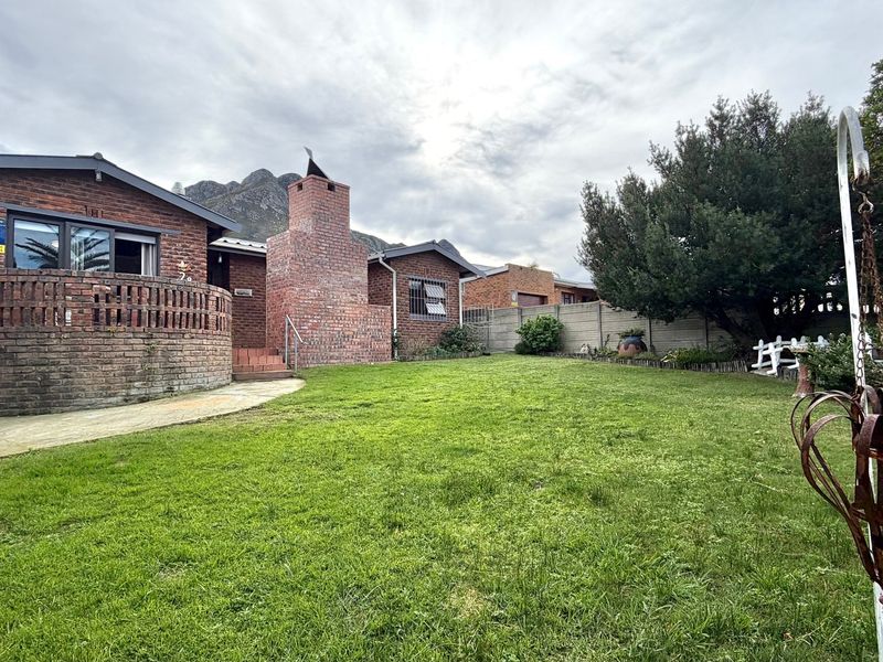 Rear view of the property featuring a brick facade, a built-in outdoor fireplace, a paved walkway, and a spacious lawn area.