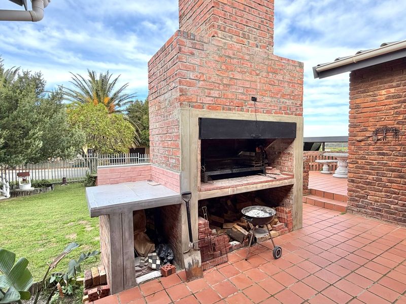 Outdoor patio area featuring a large built-in brick fireplace and braai, perfect for entertaining with direct access to the garden.