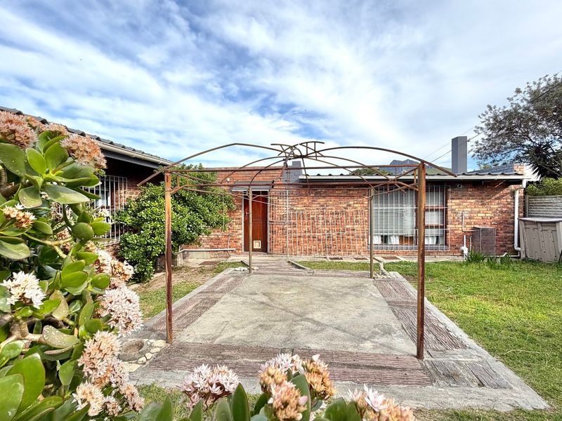 Rear exterior view featuring a brick facade, a concrete patio area with a metal pergola frame, and a private garden space.