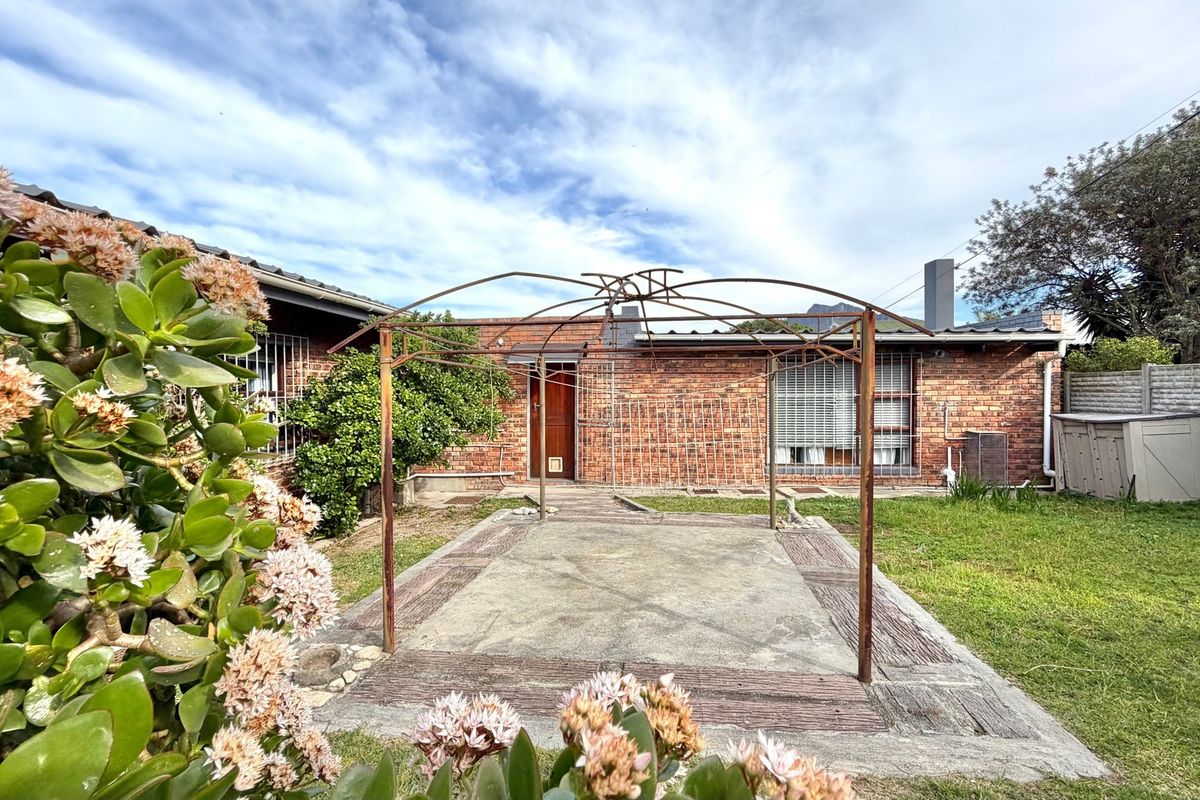 Rear exterior view featuring a brick facade, a concrete patio area with a metal pergola frame, and a private garden space.