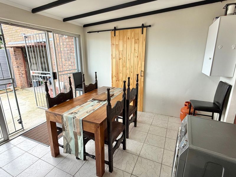 Dining area featuring tiled flooring, exposed ceiling beams, a sliding barn door, and large glass sliding doors providing access to the exterior.