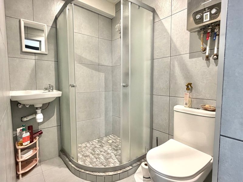 Compact bathroom featuring a corner shower enclosure, wall-mounted basin, toilet, and a wall-mounted gas water heater with tiled finishes throughout.