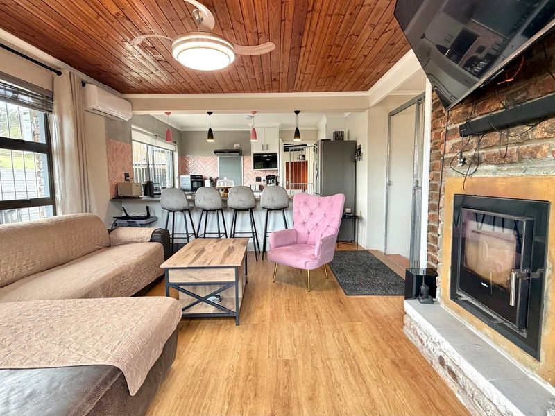 Open-plan living and kitchen area featuring a timber ceiling, brick fireplace, and a functional kitchen island with breakfast bar seating.