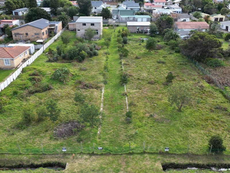 An aerial view of a vacant residential plot featuring established grass cover and perimeter fencing, situated within an established suburban neighborhood.