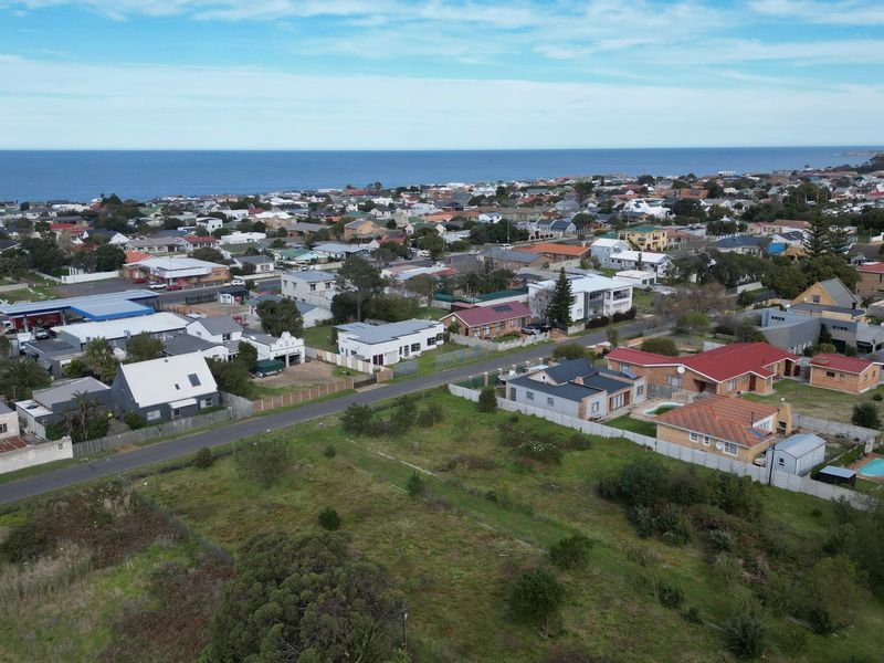 An aerial view of a vacant residential plot situated in a developed coastal neighborhood with surrounding housing and ocean views.
