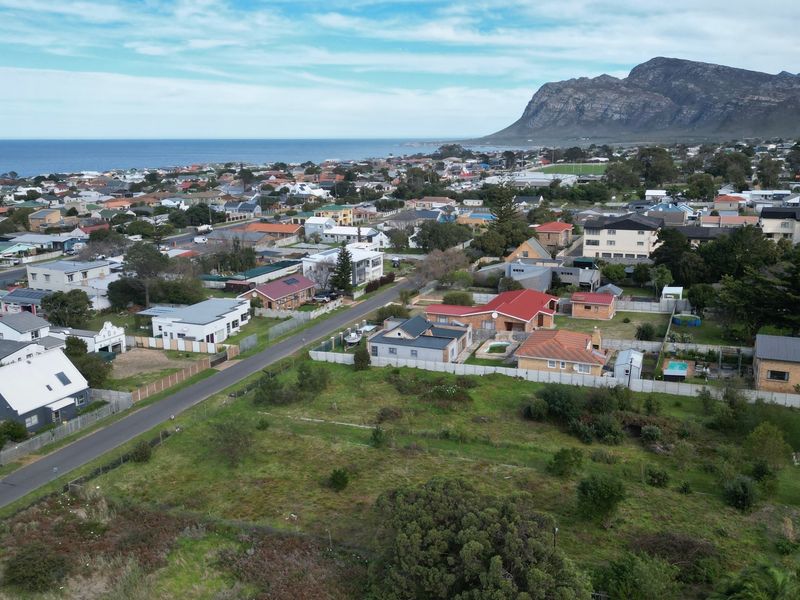An aerial view of a vacant residential plot situated within an established coastal neighborhood with mountain and sea views.