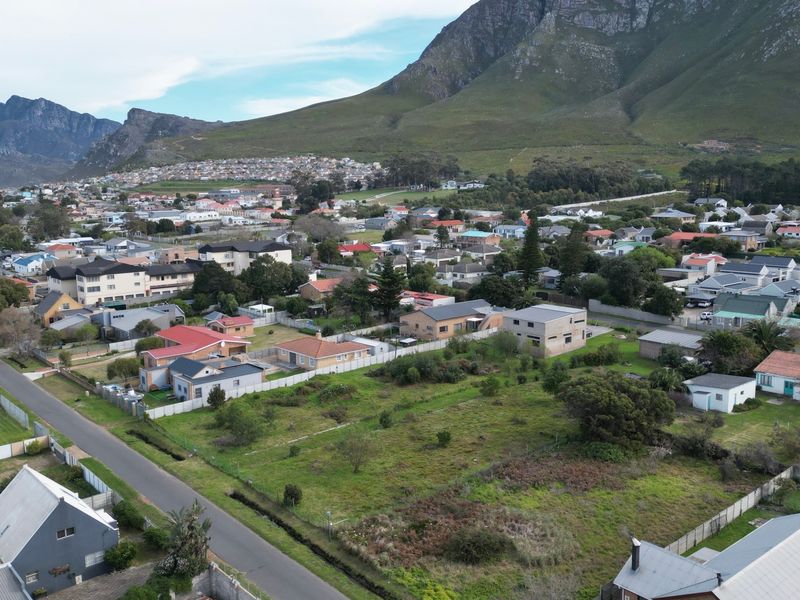 An aerial view of a vacant residential plot situated within an established neighborhood, featuring mountain views and surrounding residential infrastructure.